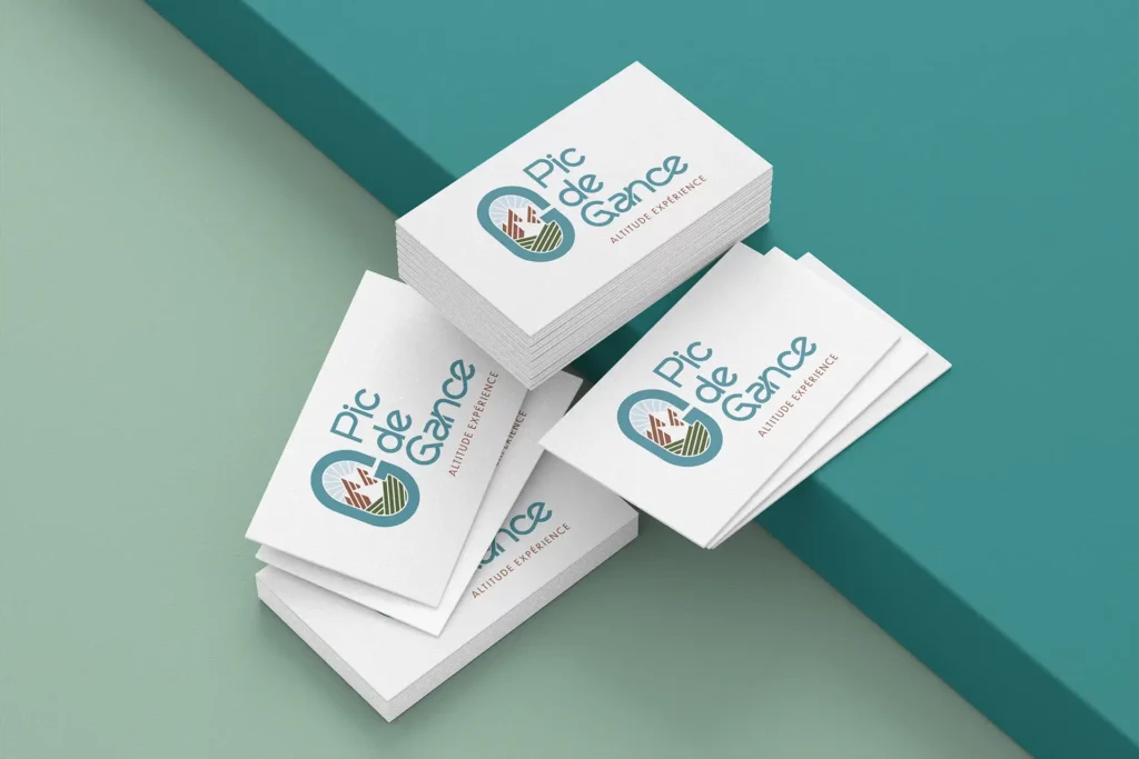 Carte de visite du logo Pic de Gance avec le slogan "Altitude Experience", posée sur une surface verte et bleue